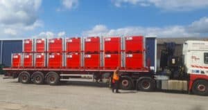 15 red steel tanks on back of a lorry with person in hi vis standing beside it. 
